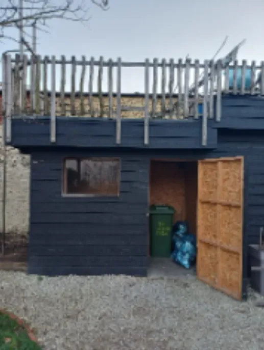 The black wooden waste shed in the shared garden